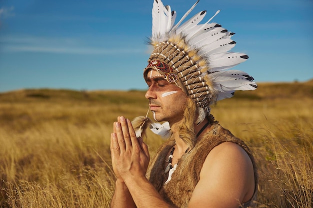 Un hombre con ropa tradicional de nativos americanos rezando en la estepa