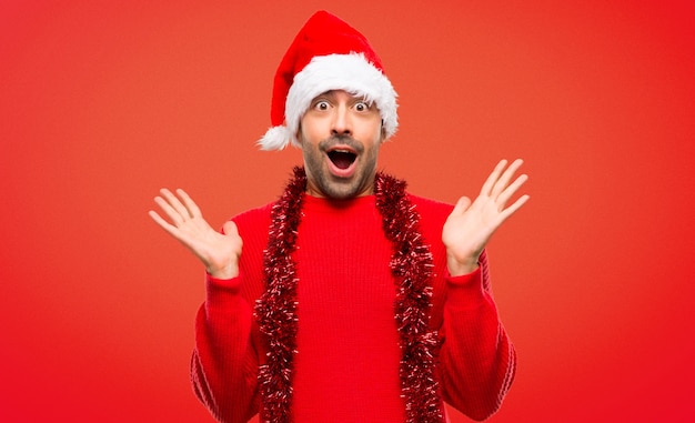 Hombre con ropas rojas celebrando las fiestas navideñas con sorpresa y conmocionado.