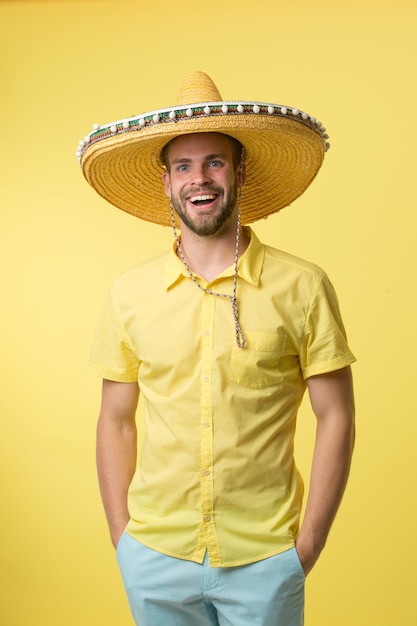 Hombre de rostro sonriente posando en sombrero sombrero con las manos en los bolsillos, fondo amarillo. Chico con cerdas parece festivo en sombrero. Concepto fest y vacaciones. Hombre de humor festivo que va a celebrar.