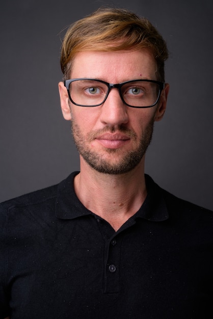 Hombre rubio con barba y gafas contra la pared gris