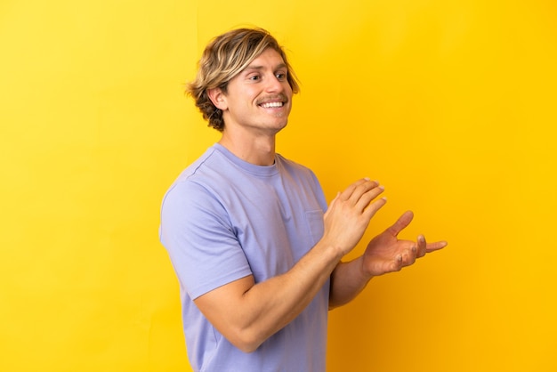 Hombre rubio guapo aislado en amarillo aplaudiendo