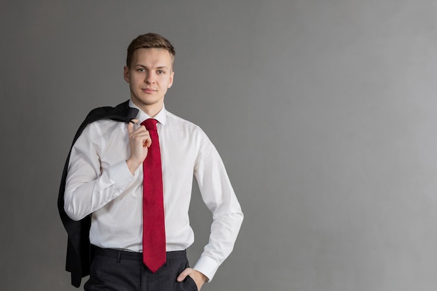 Foto hombre rubio guapo y atractivo con sonrisa en traje, corbata roja, sosteniendo un abrigo sobre su hombro