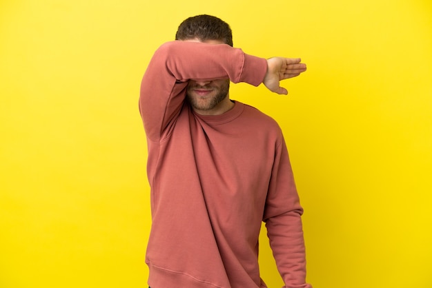 Foto hombre rubio guapo sobre fondo amarillo aislado que cubre los ojos con las manos