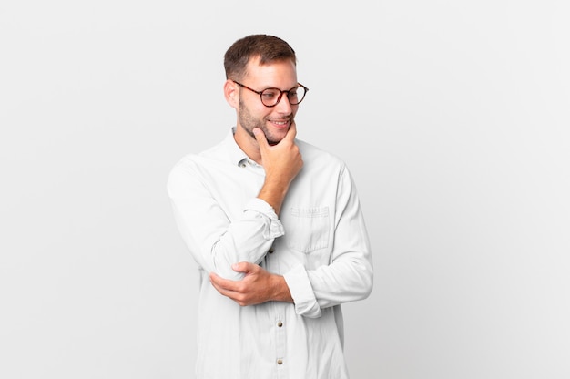 Hombre rubio guapo sonriendo con una expresión feliz y segura con la mano en la barbilla