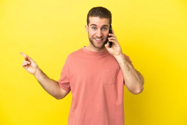 Hombre rubio guapo con teléfono móvil sobre antecedentes aislados que señala el dedo hacia el lado