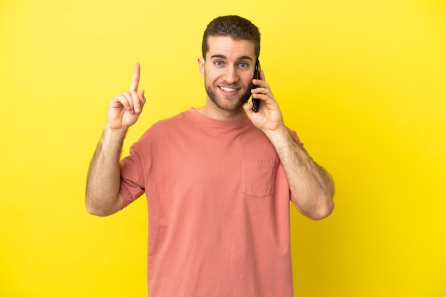 Hombre rubio guapo con teléfono móvil sobre fondo aislado apuntando hacia una gran idea