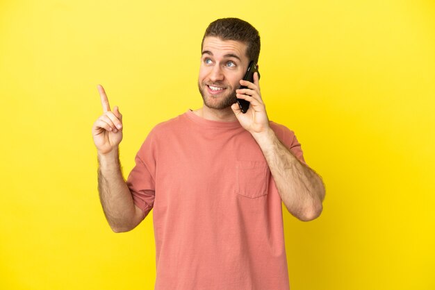 Hombre rubio guapo con teléfono móvil sobre fondo aislado apuntando hacia una gran idea