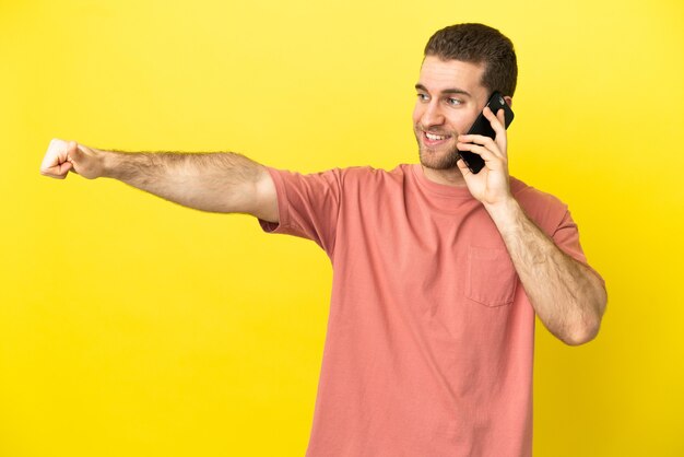 Foto hombre rubio guapo con teléfono móvil sobre fondo aislado dando un gesto de pulgar hacia arriba