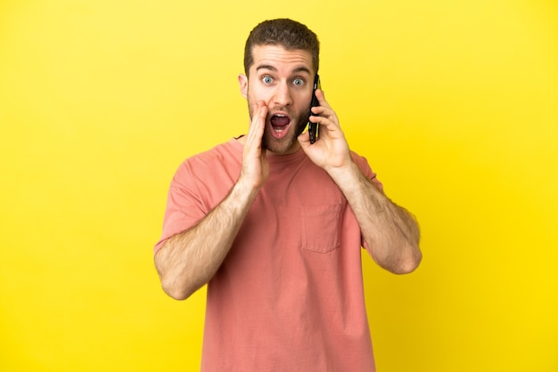 Hombre rubio guapo con teléfono móvil sobre fondo aislado con sorpresa y expresión facial conmocionada