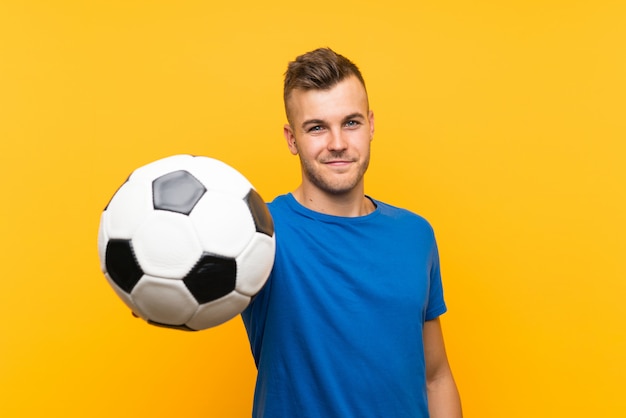 Hombre rubio hermoso joven feliz que sostiene un balón de fútbol