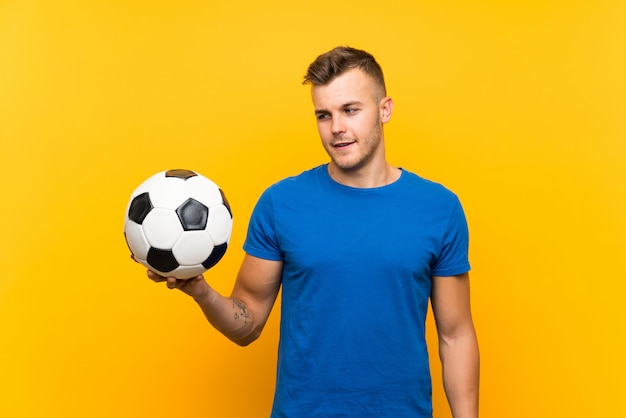 Hombre rubio hermoso joven que sostiene un balón de fútbol con expresión feliz