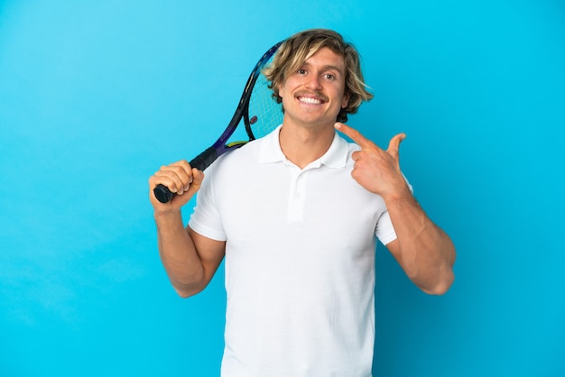 Hombre rubio jugador de tenis aislado en la pared azul dando un pulgar hacia arriba gesto