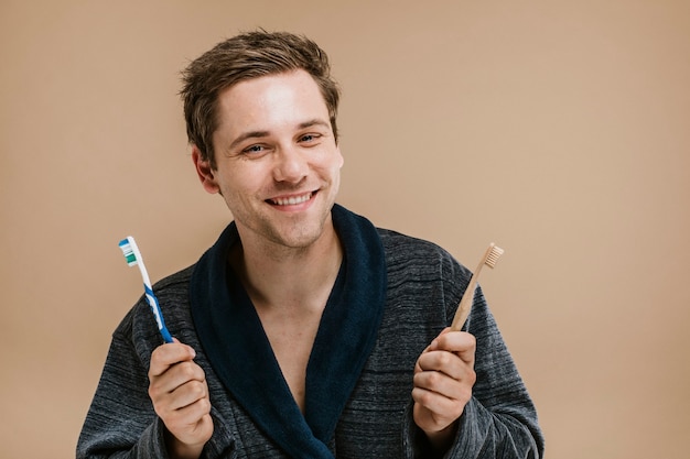 Hombre rubio con una túnica eligiendo entre un cepillo de dientes de madera y uno de plástico