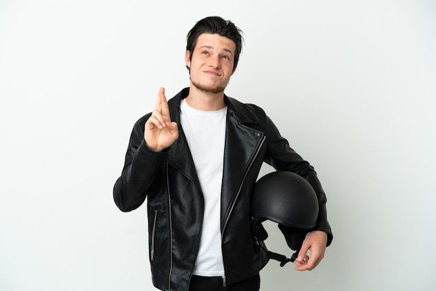 Hombre ruso con un casco de motocicleta aislado sobre fondo blanco con los dedos cruzando y deseando lo mejor