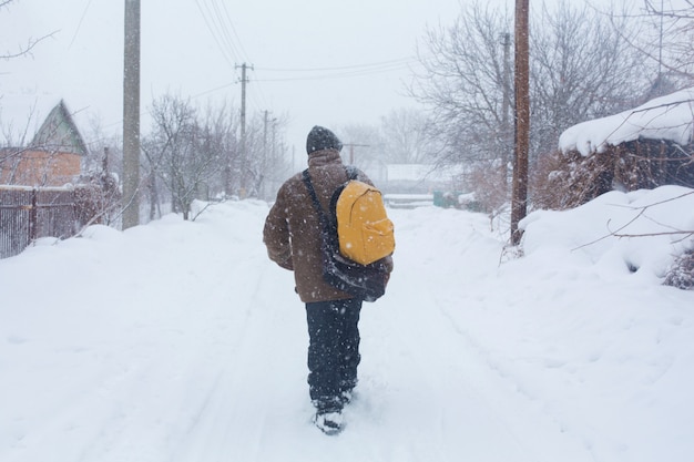 Un hombre rústico camina por la calle en invierno con una mochila amarilla. Tormenta de nieve