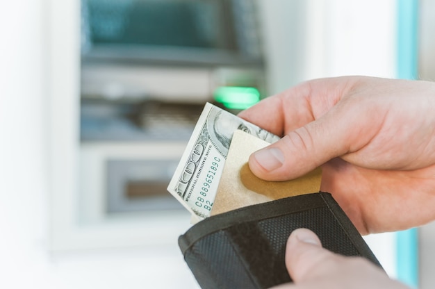 Foto el hombre saca una tarjeta bancaria con dinero de su billetera. en el contexto de un cajero automático.