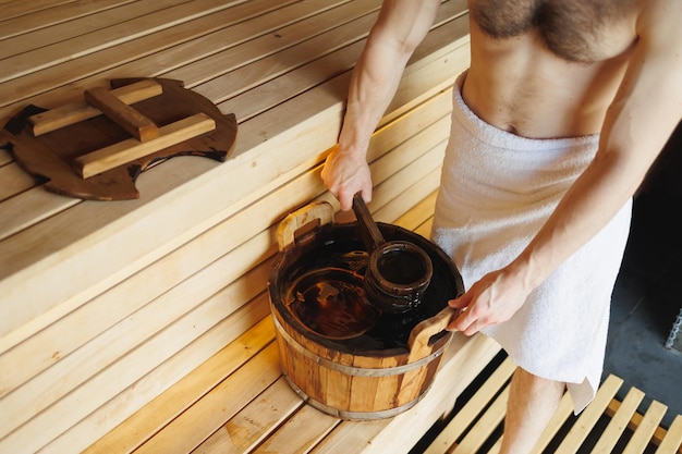 Hombre sacando agua de un cubo de madera en la sauna Descanso de spa en la sala de vapor