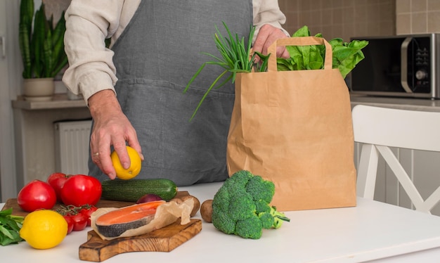 Hombre sacando comida de una bolsa de papel Verduras y verduras en una bolsa de papel en la mesa de la cocina