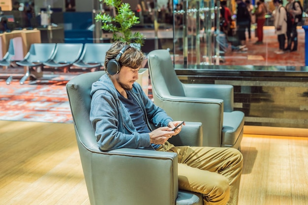 Foto un hombre en el salón del aeropuerto está esperando su avión usa un teléfono inteligente y auriculares