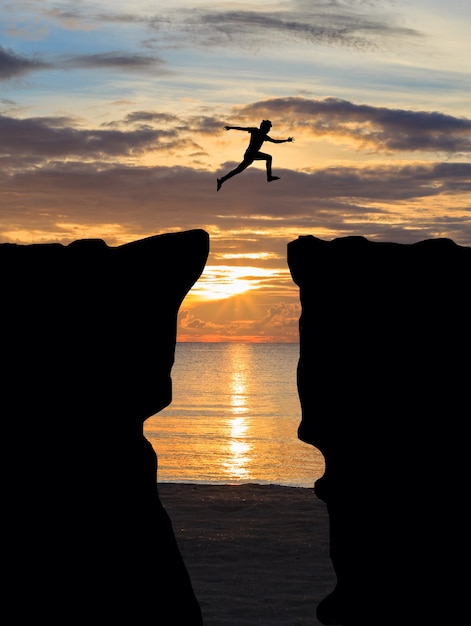 Foto hombre saltando sobre un acantilado al atardecer