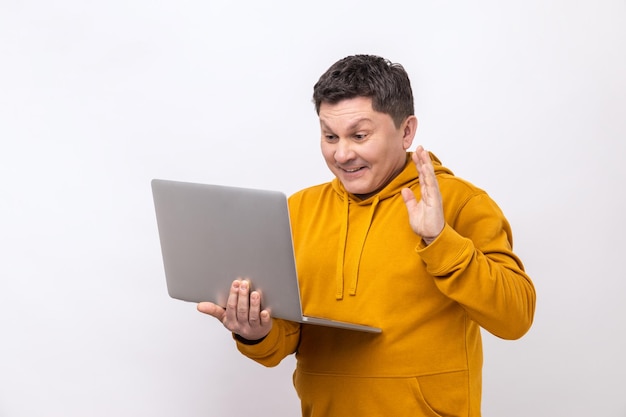 Hombre saludando con la mano saludando a la pantalla del portátil hablando por videollamada con un compañero de trabajo