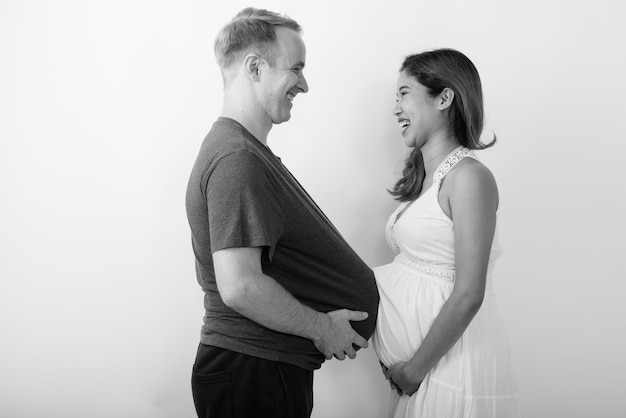 Hombre con sandía como estómago y mujer asiática embarazada juntos como matrimonio multiétnico en blanco y negro