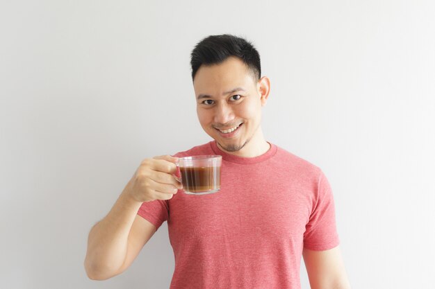 El hombre sano feliz en camiseta roja bebe el café o la bebida asiática de las hierbas.