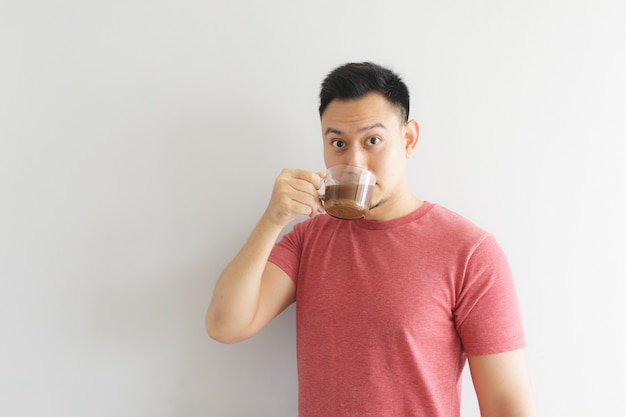 El hombre sano feliz en camiseta roja bebe el café o la bebida asiática de las hierbas.