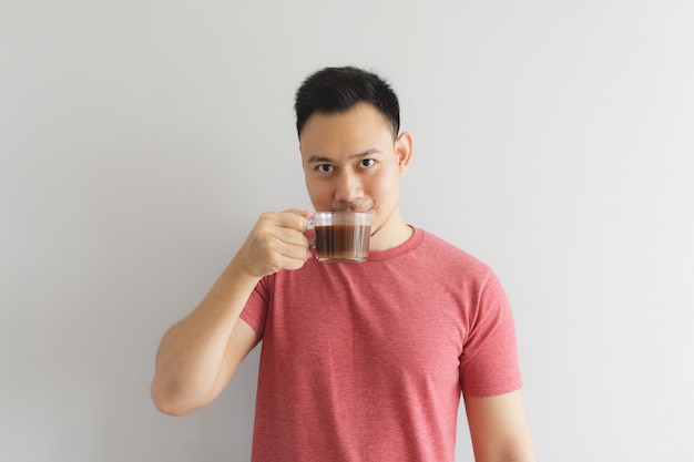 El hombre sano feliz en camiseta roja bebe el café o la bebida asiática de las hierbas.