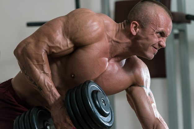 Foto hombre sano haciendo ejercicios de espalda en el gimnasio con mancuernas