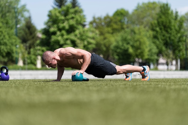 Hombre sano haciendo flexiones sobre el césped con pesas rusas