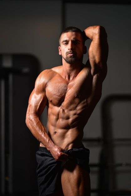 Hombre sano de pie fuerte en el gimnasio y flexionando los músculos Muscular culturista atlético modelo de fitness posando después de los ejercicios