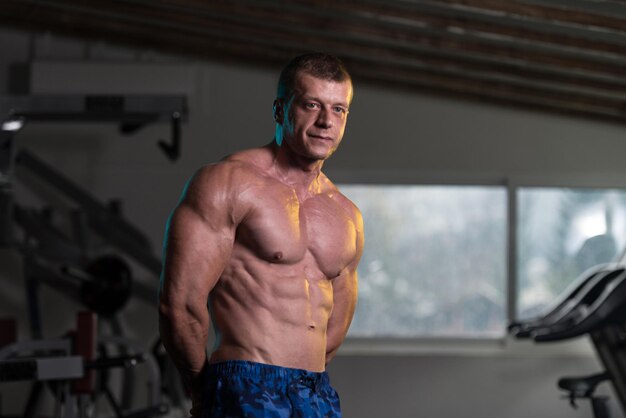 Hombre sano de pie fuerte en el gimnasio y flexionando los músculos Muscular culturista atlético modelo de fitness posando después de los ejercicios