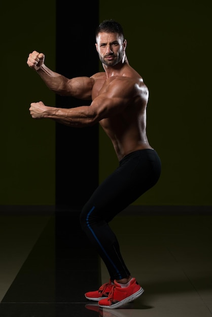 Hombre sano de pie fuerte en el gimnasio y flexionando los músculos Muscular culturista atlético modelo de fitness posando después de los ejercicios