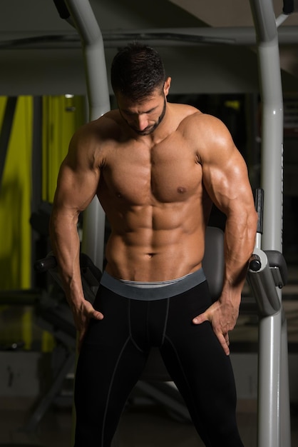 Hombre sano de pie fuerte en el gimnasio y flexionando los músculos Muscular culturista atlético modelo de fitness posando después de los ejercicios