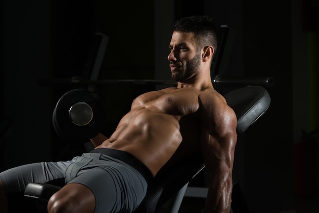 Hombre sano trabajando bíceps en un gimnasio oscuro rizos de concentración con mancuernas