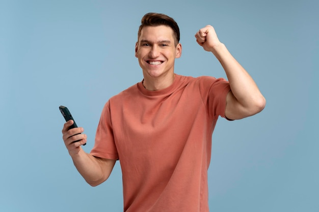 Hombre satisfecho feliz en camiseta sosteniendo teléfono inteligente y sonriendo haciendo gesto de sí