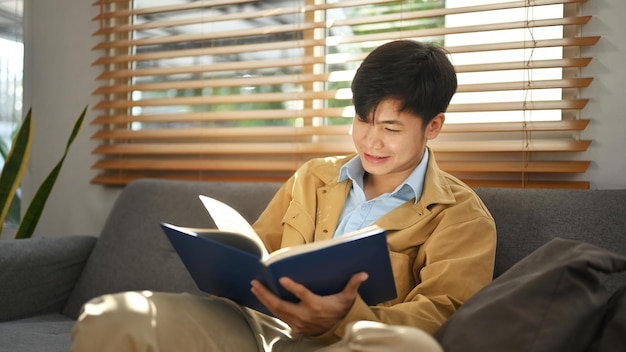 Hombre satisfecho leyendo un libro relajándose en un cómodo sofá en casa Actividad de ocio concepto de estado de ánimo positivo