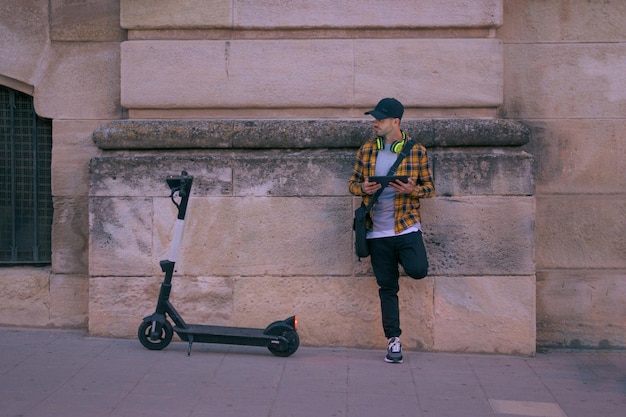 El hombre con un scooter eléctrico trabaja de forma remota con una tableta por la noche