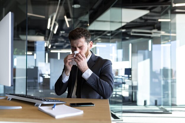 Un hombre con secreción nasal y fiebre trabaja en la oficina. Un hombre de negocios enfermo en la computadora tiene secreción nasal.