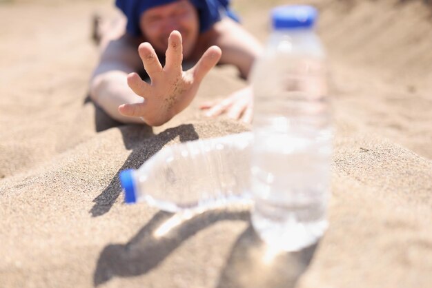 Un hombre sediento yace en la arena buscando una botella de agua.