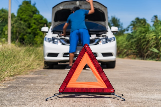 Un hombre y una señal de paro de emergencia roja y un coche blanco problema en la carretera