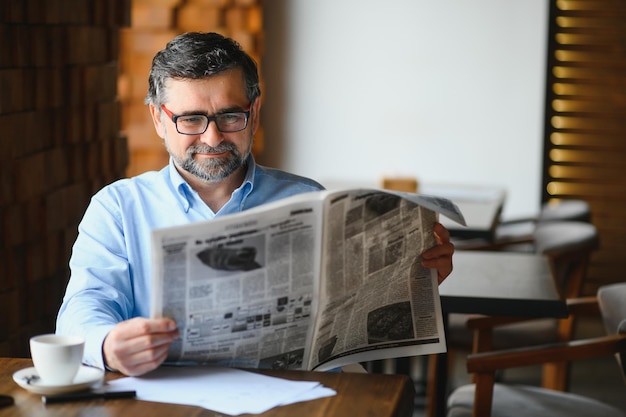 Hombre senior activo leyendo el periódico y bebiendo café en el restaurante