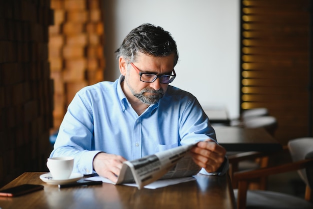 Hombre senior activo leyendo el periódico y bebiendo café en el restaurante