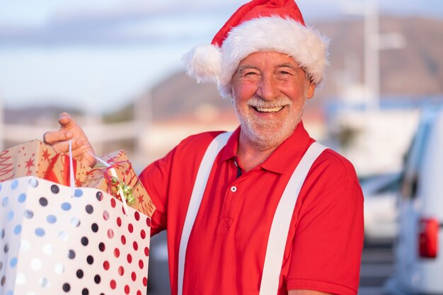 Hombre senior alegre de compras para la Navidad en un gorro de Papá Noel sosteniendo una bolsa llena de regalos