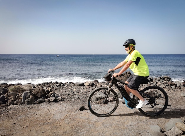 Hombre senior en bicicleta al aire libre en el mar disfrutando de la libertad y un estilo de vida saludable