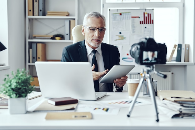 Hombre senior en elegante traje de negocios usando tableta digital mientras hace videos de redes sociales