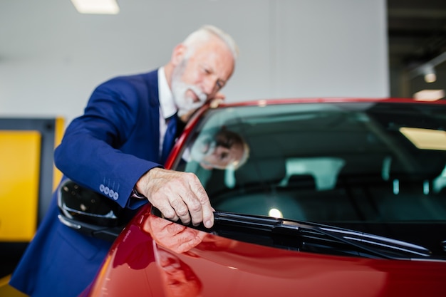 Hombre Senior eligiendo un coche nuevo en la sala de exposición de coches.