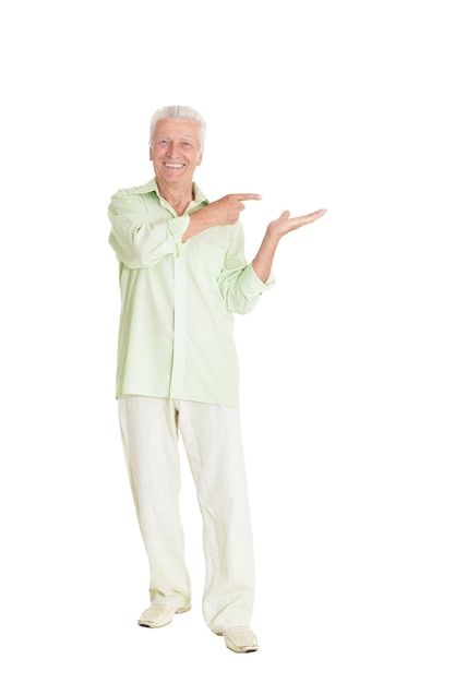 Hombre senior feliz en camisa verde apuntando a la derecha sobre fondo blanco.