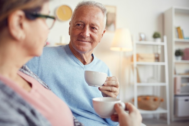 Hombre senior feliz charlando con su esposa sobre una taza de té